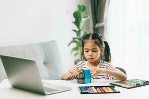 carino asiatico poco bambino ragazza utilizzando il computer portatile e fare compiti a casa a casa foto
