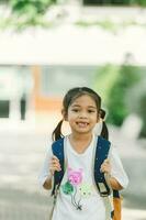 poco asiatico ragazza andando indietro per scuola con zaino e contento sorridente. foto