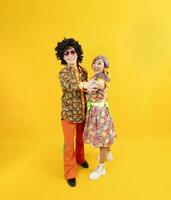 asiatico hippie coppia vestito nel anni 80 Vintage ▾ moda con colorato retrò capi di abbigliamento mentre danza insieme isolato su giallo sfondo per fantasia attrezzatura festa e pop cultura foto