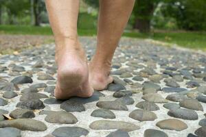 a piedi nudi vecchio uomo passo su pietre, piede riflessologia a il concetto.parco di piede massaggio per aumentare sangue circolazione nel anziani, sollievo per stanco e dolorante piedi foto