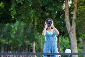 asiatico ragazza usi binocolo per osservare il natura, uccelli, e animali di il nazionale parco mentre campeggio con sua famiglia. con il concetto di apprendimento al di fuori il aula natura studia, esplorazione. foto