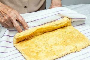 vicino su di un' anziano donna mani rotolamento un' appena al forno spugna torta foto