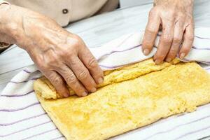 vicino su di un' anziano donna mani rotolamento un' appena al forno spugna torta foto