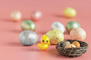 uova di pasqua in un nido naturale con uova di uccelli. uova dipinte e un pollo decorativo su uno sfondo rosa di colori pastello. messa a fuoco selettiva