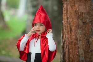 dolce ragazza indossare un' poco rosso equitazione cappuccio costume. vero famiglia avendo divertimento mentre utilizzando costumi di il poco rosso equitazione cappuccio racconto nel Halloween. foto