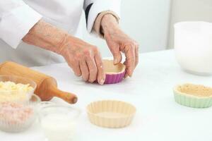 anziano donna preparazione Impasto per un' delizioso formaggio e prosciutto tortino foto