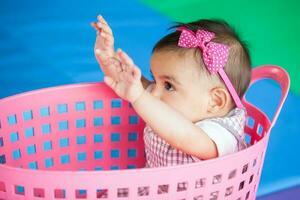 bellissimo dieci mesi bambino ragazza giocando nel un' rosa cestino. presto stimolazione per bambini piccoli concetto. foto