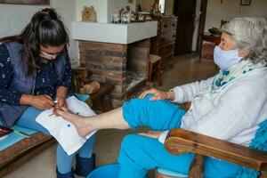 pedicurist fabbricazione un' pedicure per un' anziano donna a casa durante covid 19 pandemia indossare viso maschera foto