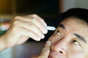 asiatico uomo usi artificiale lacrima lubrificante occhio gocce con il suo occhi. concetto, assistenza sanitaria. trattamento per asciutto occhio sintomi, occhio infiammazione malattie. sollievo irritata ottica. foto