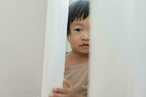 poco asiatico bambini ragazzo , giocando nascondere e cercare in piedi Il prossimo un' parete Casa, adorabile bambino avendo divertimento nel il casa. contento famiglia avere divertimento con bambini, attività, apprendimento foto