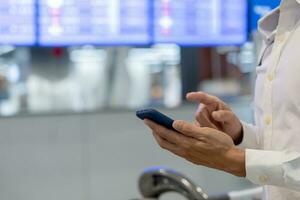 attività commerciale uomo utilizzando mobile Telefono per libro aereo biglietto attraverso in linea applicazione, seduta su viaggio controllo viaggio tempo su tavola a aeroporto, viaggiare, pagamento, dovuto, prenotazione, in linea, dai un'occhiata nel foto