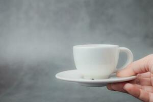 mano Tenere bianca tazza di caffè con piattino su buio sfondo foto