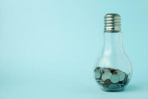 monete nel leggero lampadina bottiglia forma su blu sfondo foto