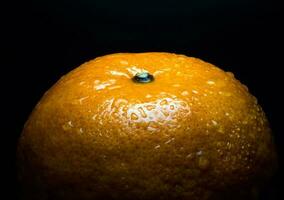 goccia d'acqua sulla superficie lucida di freschezza arancione su sfondo nero foto