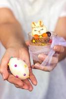 le mani della donna che tengono una tazza di plastica trasparente con mousse al cioccolato in una mano e uovo di Pasqua decorato nell'altra foto