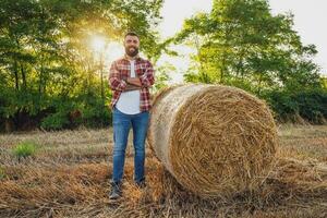 contadino è in piedi accanto balle di fieno. lui è soddisfatto dopo riuscito raccolta. foto