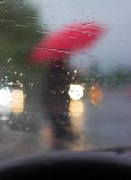 al volante - sagoma di un uomo con ombrello rosso, foto scattata dall'auto, dietro il parabrezza