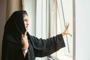 arabo donna nel nero hijab guardare su il finestra foto