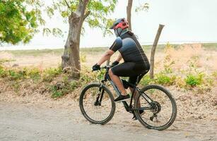 paffuto ciclista su il strada. professionale ciclista su un' sporco strada, Grasso ciclista su un' sporco strada circondato di alberi foto