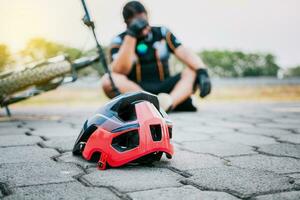 incidentato ciclista seduta su il marciapiede. concetto di incidentato ciclista con casco su il marciapiede nel primo messa a fuoco foto