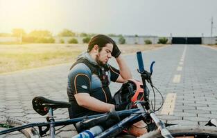 maschio ciclista seduta con male alla testa. ciclista su il marciapiede con un' male alla testa. concetto di ciclista sofferenza con emicrania foto