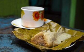 tradizionale Tamal pisque ripieno con un' tazza di caffè servito su il tavolo. Tamal pisque ripieno tipico nicaraguense cibo. Visualizza di un' ripieno tamale con un' tazza di caffè servito su un' di legno tavolo foto