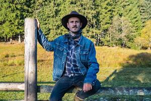 cowboy in giacca di jeans e cappello vicino al recinto in montagna foto