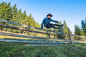 cowboy in giacca di jeans e cappello vicino al recinto in montagna foto