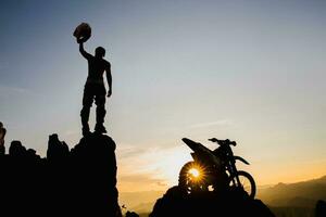 uomo con motocross bicicletta contro bellissimo luci, silhouette di un' uomo con motocross motociclo su superiore di roccia alto montagna a bellissimo tramonto, enduro motociclo viaggio concetto. foto