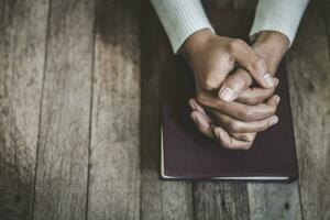 mano di donna mentre preghiere per cristiano religione, casuale donna preghiere con sua mani insieme al di sopra di un' chiuso Bibbia. foto