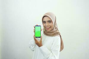 eccitato bellissimo asiatico musulmano donna mostrando verde schermo mobile Telefono isolato al di sopra di bianca sfondo foto