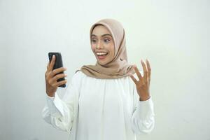 eccitato bellissimo asiatico musulmano donna mostrando mobile Telefono isolato al di sopra di bianca sfondo foto