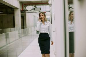 giovane attività commerciale donna utilizzando mobile Telefono nel il ufficio corridoio foto