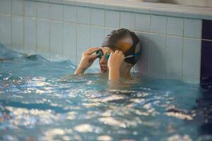 ragazzo nel un' nuoto berretto e nuoto occhiali nel il piscina. il bambino è impegnato nel il nuoto sezione. foto