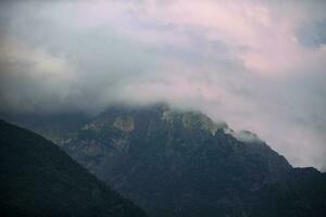 buio atmosferico surreale paesaggio con un' buio roccioso montagna picco nel Basso nuvole nel un' grigio nuvoloso cielo. un' grigio Basso nube su un' alto picco. alto nero roccia nel Basso nuvole. surreale cupo montagne. foto