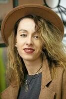 un' bellissimo ragazza nel un' beige elegante cappello con lungo Riccio capelli sembra a il telecamera e sorrisi. foto