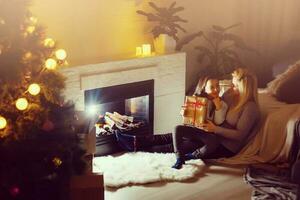 giovane madre e le sue due figlie che aprono un magico regalo di Natale da un albero di Natale nell'accogliente soggiorno in inverno foto