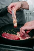 cucinando bistecche nel un' padella. cucinando Manzo a il culinario maestro classe. il mani di il capocuoco nel nero guanti. foto