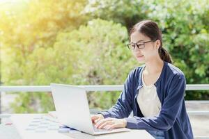 Università adolescente asiatico giovane donna seduta formazione scolastica apprendimento digitando il computer portatile computer con verde albero sfondo. foto