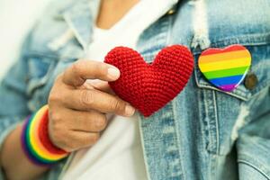 la signora asiatica che indossa braccialetti con bandiera arcobaleno e tiene il cuore rosso, simbolo del mese dell'orgoglio lgbt celebra l'annuale a giugno sociale di gay, lesbiche, bisessuali, transgender, diritti umani. foto