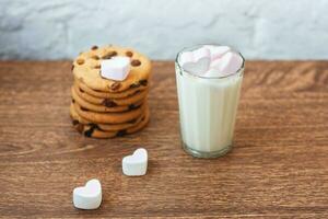 fragranti, gustosi biscotti fatti in casa con uvetta, marshmallow a forma di cuore e un bicchiere di latte fresco in tavola foto