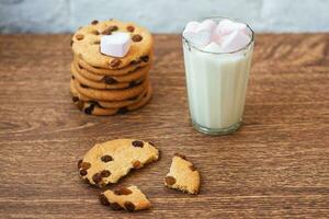 fragranti, gustosi biscotti fatti in casa con uvetta, marshmallow a forma di cuore e un bicchiere di latte fresco in tavola foto