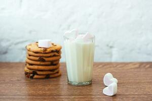 fragranti, gustosi biscotti fatti in casa con uvetta, marshmallow a forma di cuore e un bicchiere di latte fresco in tavola foto