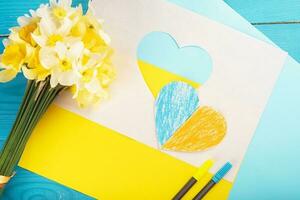 cuore ritagliato di carta e dipinto nei colori blu e giallo e fiori primaverili gialli sul dorso in legno. creatività foto