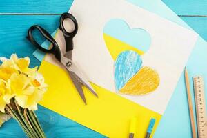 cuore ritagliato di carta e dipinto nei colori blu e giallo e fiori primaverili gialli sul dorso in legno. creatività foto