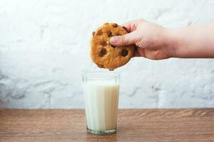 ragazzo che immerge gustoso biscotto in un bicchiere di latte. fragranti, gustosi biscotti fatti in casa con uvetta e un bicchiere di latte fresco foto