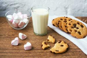 biscotti fatti in casa con latte e marshmallow d'aria su asciugatutto e tavolo di legno. Buongiorno. concetto di colazione foto