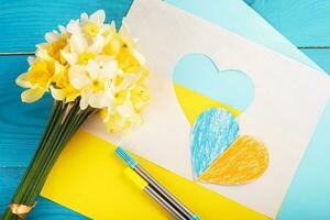 cuore ritagliato di carta e dipinto nei colori blu e giallo e fiori primaverili gialli sul dorso in legno. creatività foto