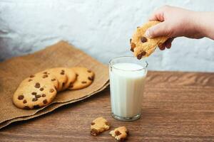 ragazzo che immerge gustoso biscotto in un bicchiere di latte. fragranti, gustosi biscotti fatti in casa con uvetta e un bicchiere di latte fresco foto