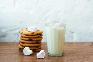 fragranti, gustosi biscotti fatti in casa con uvetta, marshmallow a forma di cuore e un bicchiere di latte fresco in tavola foto